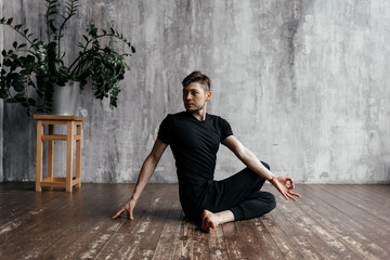 A young man performing yoga asanas and sports exercises to improve the strength and flexibility of...