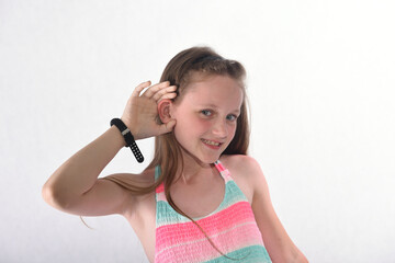 A beautiful school-age girl in the studio on a white background stands forward and holds her ear...