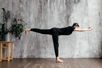 A young man performing yoga asanas and sports exercises to improve the strength and flexibility of...