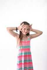 A beautiful school-age girl in the studio on a white background plays scenes with palms and fingers...