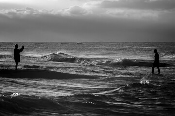 a woman takes a picture of a man standing in the sea.a black and white picture