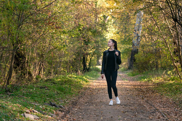 Girl walks in the autumn park. Young beautiful woman in black clothes in the forest. Alley, promenade.