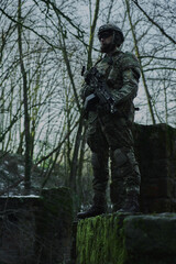 Portrait of airsoft player in professional equipment with machine gun in the forest. Soldier with weapons at war