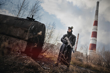 Post apocalypse soldier with a rifle and in the gas mask on the factory chimney background.