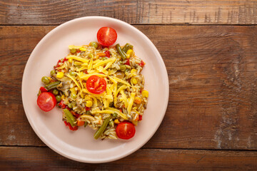 Risotto with mushrooms and vegetables in a plate on a wooden background.