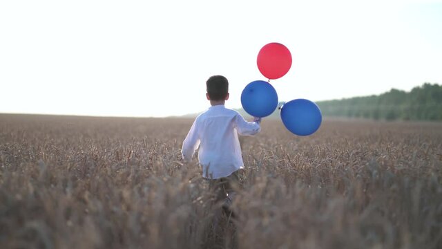 Cute boy running in the wheat field with balloons