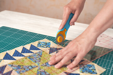 Home craft concept photo - woman hands, cutting textile for patchwork or quilt  on a mat with rotary cutter and ruler.
