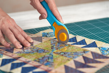 Home craft concept photo - woman hands, cutting textile for patchwork or quilt  on a mat with rotary cutter and ruler. - obrazy, fototapety, plakaty