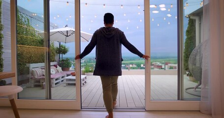 man opens sliding doors, going out on rooftop patio with cozy lounge zone and beautiful landscape view - Powered by Adobe