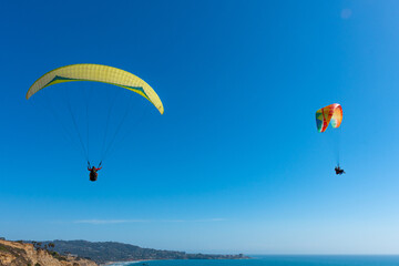 Fototapeta na wymiar Paragliders with the beautiful blue open ocean, waves, and water behind them. Location near blacks beach, San Diego County, California.