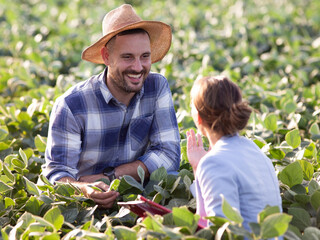 Handsome farmer talking to young insurance sales rep in soy field.