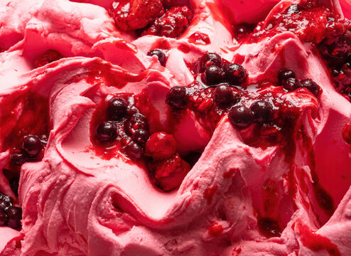 Frozen Forest Fruits flavour gelato - full frame detail. Close up of a pink surface texture of Ice cream covered with pieces of red fruit.