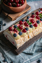 airy meringue cake with cherries on a brown board