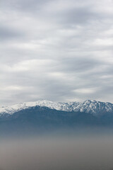 Fototapeta na wymiar Mountain top covered in snow above the pollution clouds of urban area city in Santiago, Chile