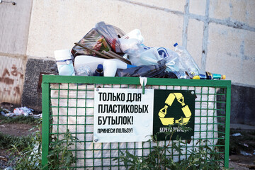 an overflowing green garbage container for collecting plastic waste and bottles against the background of the concrete wall of the building
