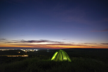 Fototapeta na wymiar Morning landscape, tent against the backdrop of the sunset and city lights on a hill in Ukraine