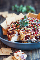 Front view of fresh homemade cranberry cheese spread made with cream cheese, cheddar, dried cranberries, pecans, and chives. Garnished with oregano over rustic wood background. Ready for the holidays