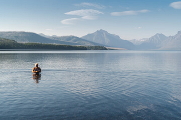 Fototapeta na wymiar Blonde adult woman enjoys taking a dip in the cold waters of Lake McDonald in Glacier National Park during a heatwave