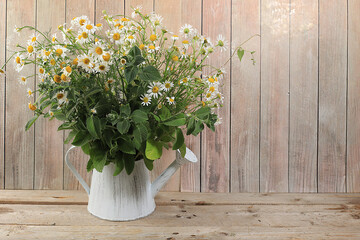 Abstract flower arrangement, background, minimal holiday concept with flowers, autumn-summer banner. Chamomile flowers in a watering can on a wooden background, rustic style, postcard 