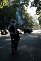 man on bicycle holding Argentine flag