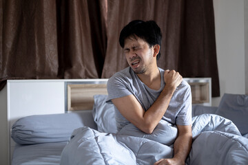 Fototapeta premium Young asian man with shoulder pain in bedroom, health problems