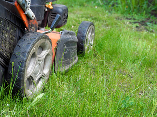 the lawn mower is standing on the green grass . rear view . gardening