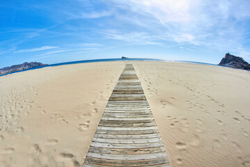 wooden path to the sea on the beach in benidorm. An island in the background.