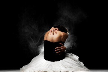 ballerina with a tutu sitting on the floor, posing with smoke in the background