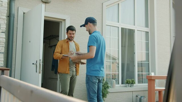 Delivery worker is bringing package to male customer's house giving box standing outside at front door. Occupation and postal service concept.