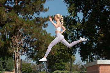 Healthy and fit atrractive blonde woman leaping to the left over obstacles at the park while looking forward