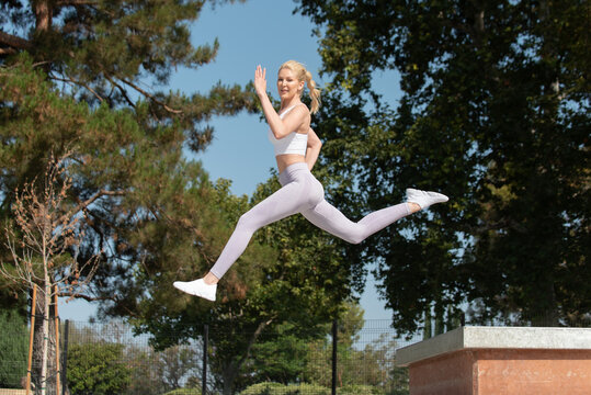 Healthy And Fit Atrractive Blonde Woman Leaping To The Left Over Obstacles At The Park While Looking Ahead