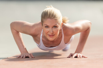 Healthy and fit atrractive blonde woman shows the core and arm strength to hold a push up in lowest...