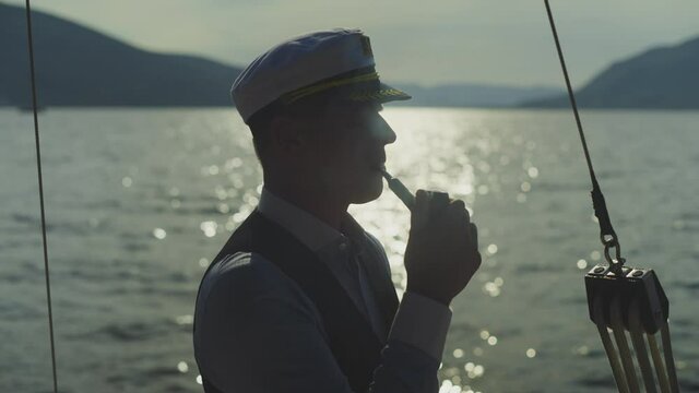 Sailor enjoying evening on sea with smoking tobacco pipe. Glittering water surface. Summer vacation at sea, sailing and travelling concept.