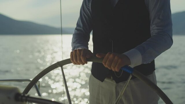 Male hands turning with steering wheel on boat. Man driving yacht on water. Summer vacation at sea, sailing and travelling concept.