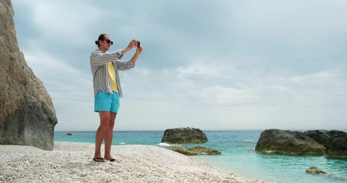 Young tourist man taking pictures of beautiful beach with smartphone.