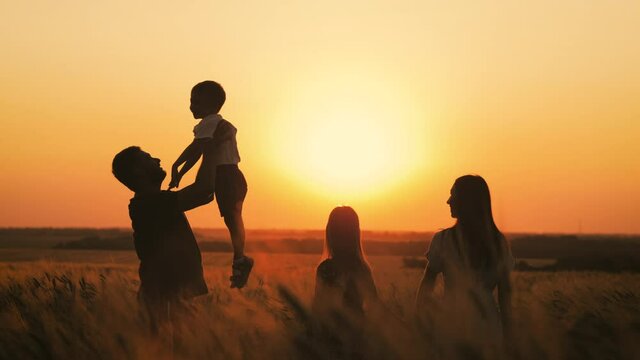 Silhouette happy family. Father having fun tossing up son. People playing enjoying sunset in wheat field on summer day. Beautiful sunset on a wheat field. Friendly family and teamwork concept.