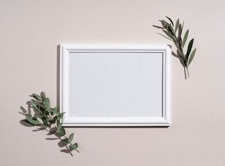 Picture frame mockup with white wooden frame. Eucalyptus leaves on beige background.