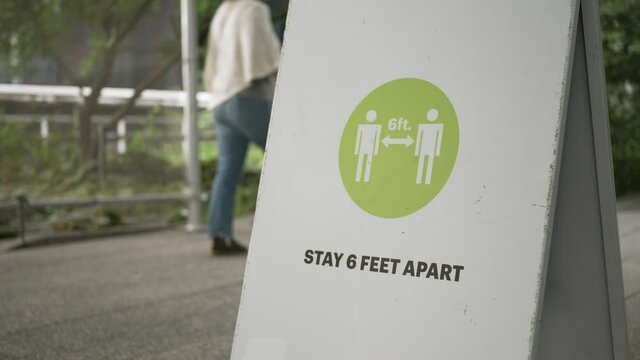 A closeup view of a social distance sign on The High Line as tourists walk by. Social distancing was a common practice to reduce the spread of COVID-19.  	