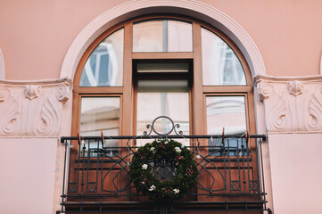 A Christmas wreath hangs on the wrought-iron railing of a balcony with a semicircular window.