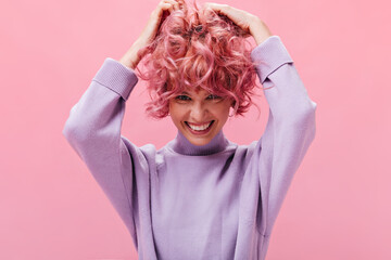 Cute young girl ruffles curly pink hair on isolated background. Pretty short-haired woman in purple...