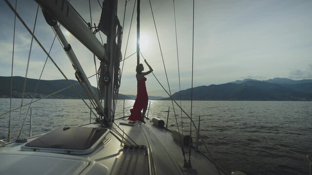 Silhouette of attractive woman standing on sailboat deck. Romantic view in sunset time. Summer vacation at sea, sailing and travelling concept.