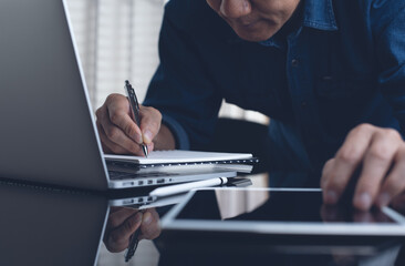 Student studying online class via laptop computer and writing on notebook