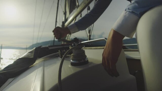 Close-up of male hand turning with winch handle to adjust sails. Cruising on sailboat. Summer vacation at sea, sailing and travelling concept.