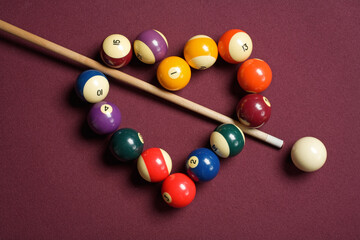 Pool cue stick bisecting heart-shaped billiard balls on billiard table