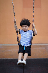 Happy little Asian boy having fun on the swing at the playground.