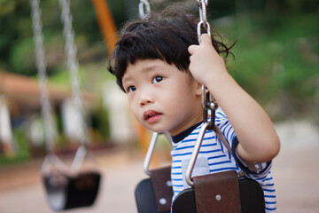 Happy little Asian boy having fun on the swing at the playground.