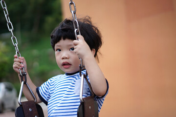 Happy little Asian boy having fun on the swing at the playground.