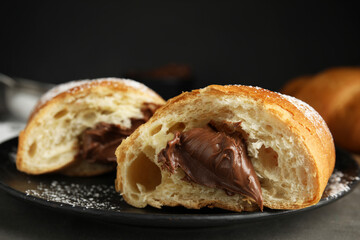 Tasty croissant with chocolate and sugar powder on black plate, closeup