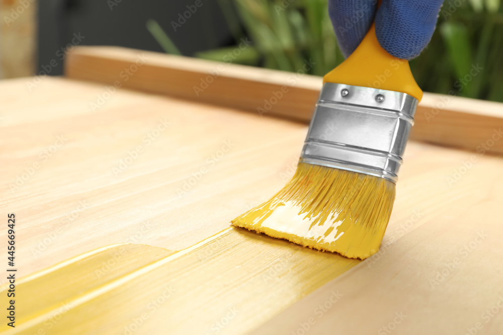 Wall mural Worker applying yellow paint onto wooden surface, closeup. Space for text