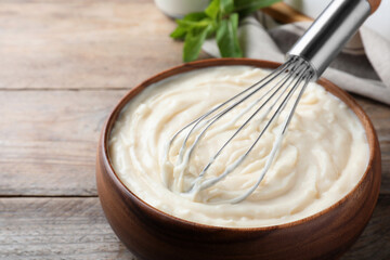 Whipping pastry cream with balloon whisk on wooden table, closeup